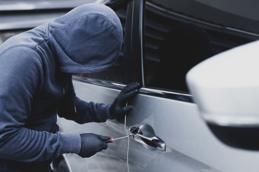 Car thief hand holding screwdriver tamper yank and glove black stealing automobile trying door handle to see if vehicle is unlocked trying to break into inside